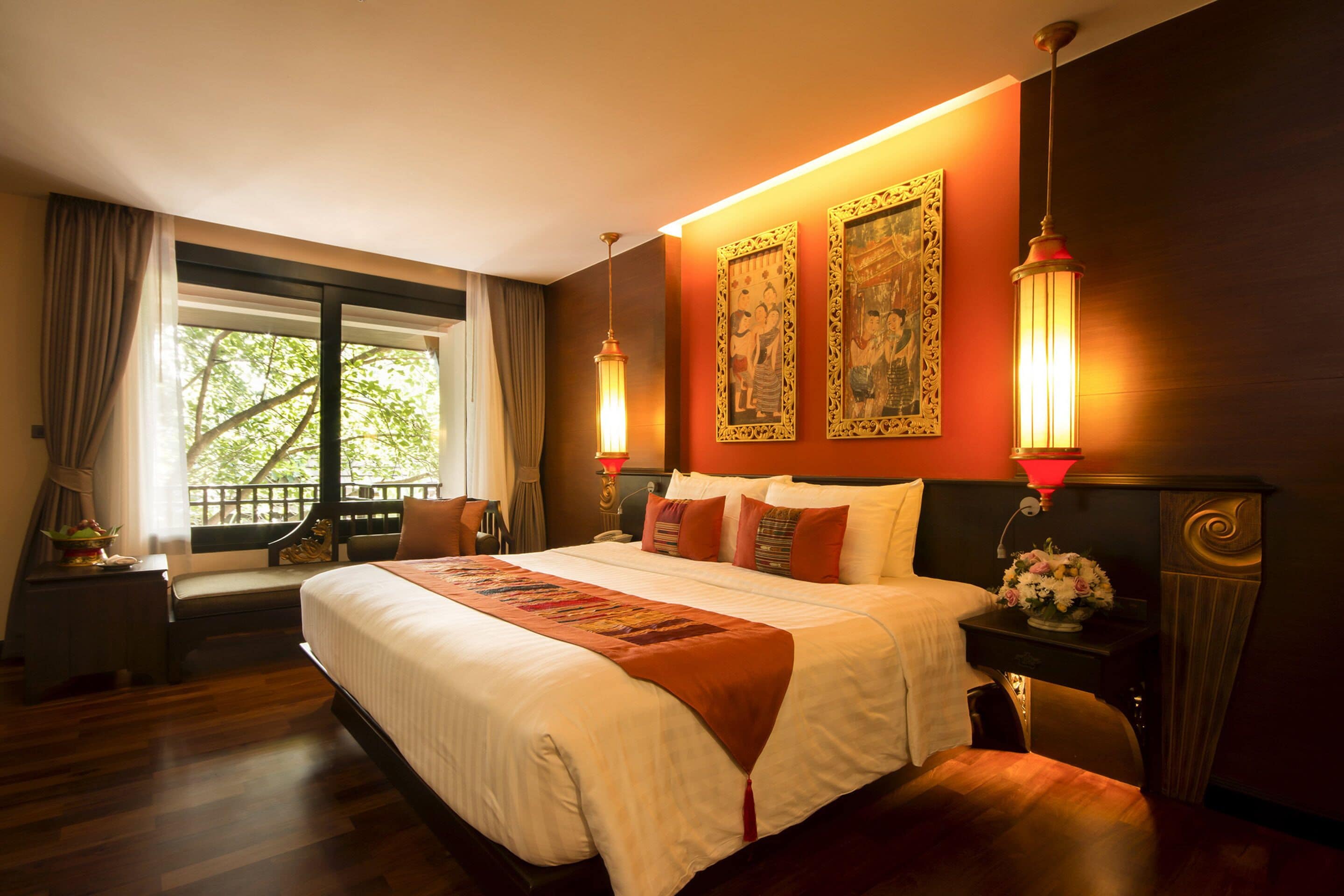 Habitación de hotel con una cama grande, una mesita de noche con lámpara, una silla y una ventana con cortinas.