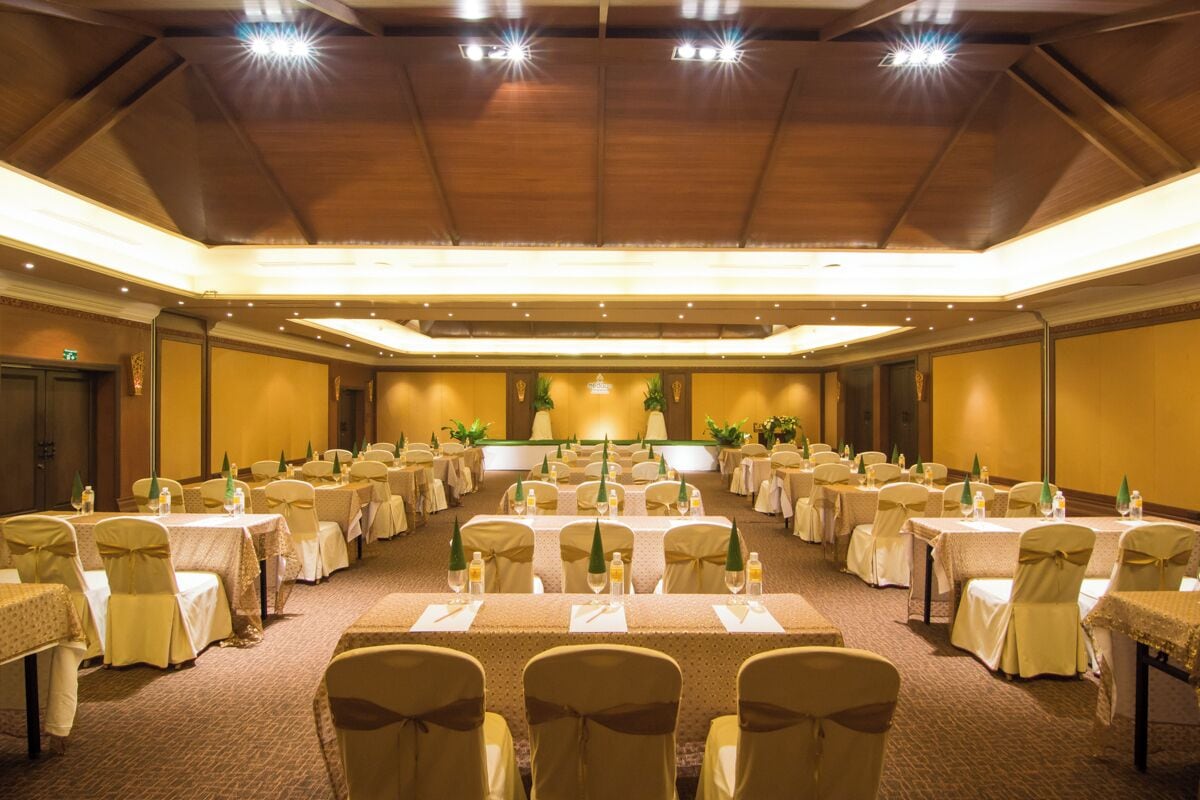 A conference room with multiple tables and chairs, arranged in rows, with a stage at the front.