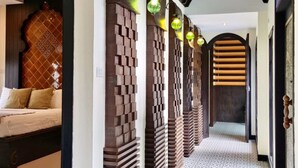 Un pasillo con baldosas de diseño, una cama con cabecera decorativa y varios apliques en la pared.