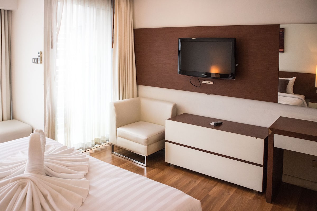 A hotel room with a large bed, a seating area, a TV mounted on the wall, and a wooden desk.