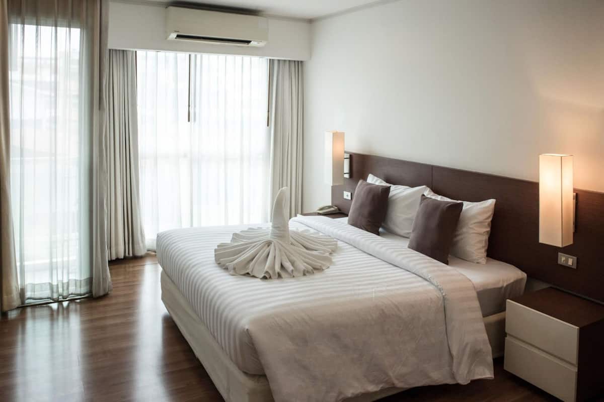 A hotel room with a large bed, a bedside table, a nightstand, and a wall-mounted lamp.