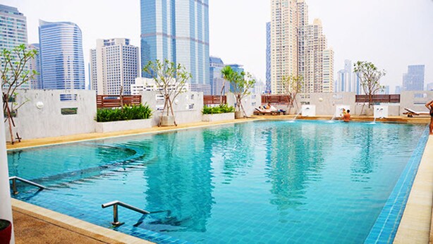 A swimming pool with a cityscape view, surrounded by greenery and lounge areas. - Sathorn Grace Serviced Residence (Bangkok)