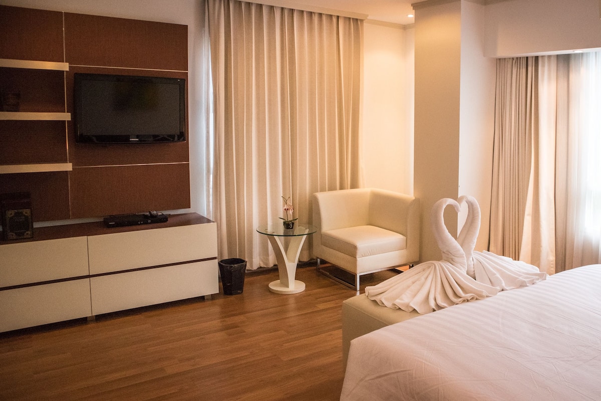 A hotel room with a bed, a TV mounted on the wall, a chair, a small table, and curtains.