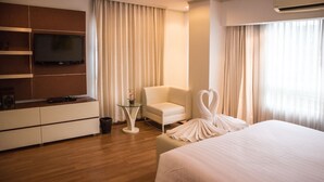 A hotel room with a bed, a TV mounted on the wall, a chair, a small table, and curtains. - Sathorn Grace Serviced Residence (Bangkok)