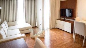 A modern living room with a sofa, a glass coffee table, a TV mounted on a wooden cabinet, and a dining area with a table and chairs. - Sathorn Grace Serviced Residence (Bangkok)
