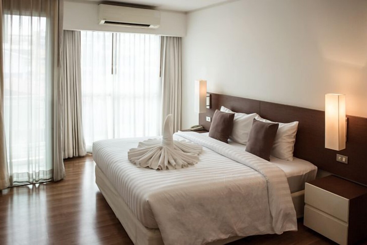 A hotel room with a large bed, bedside lamps, a nightstand, and a window with curtains.