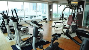 A gym with cardio machines, weight equipment, and a view of the city through large windows. - Sathorn Grace Serviced Residence (Bangkok)