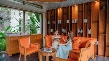 A modern interior with a wooden bookshelf, orange seating, and a view of greenery outside.