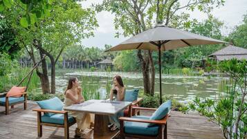 An outdoor deck with a table and chairs, surrounded by lush greenery and a pond.