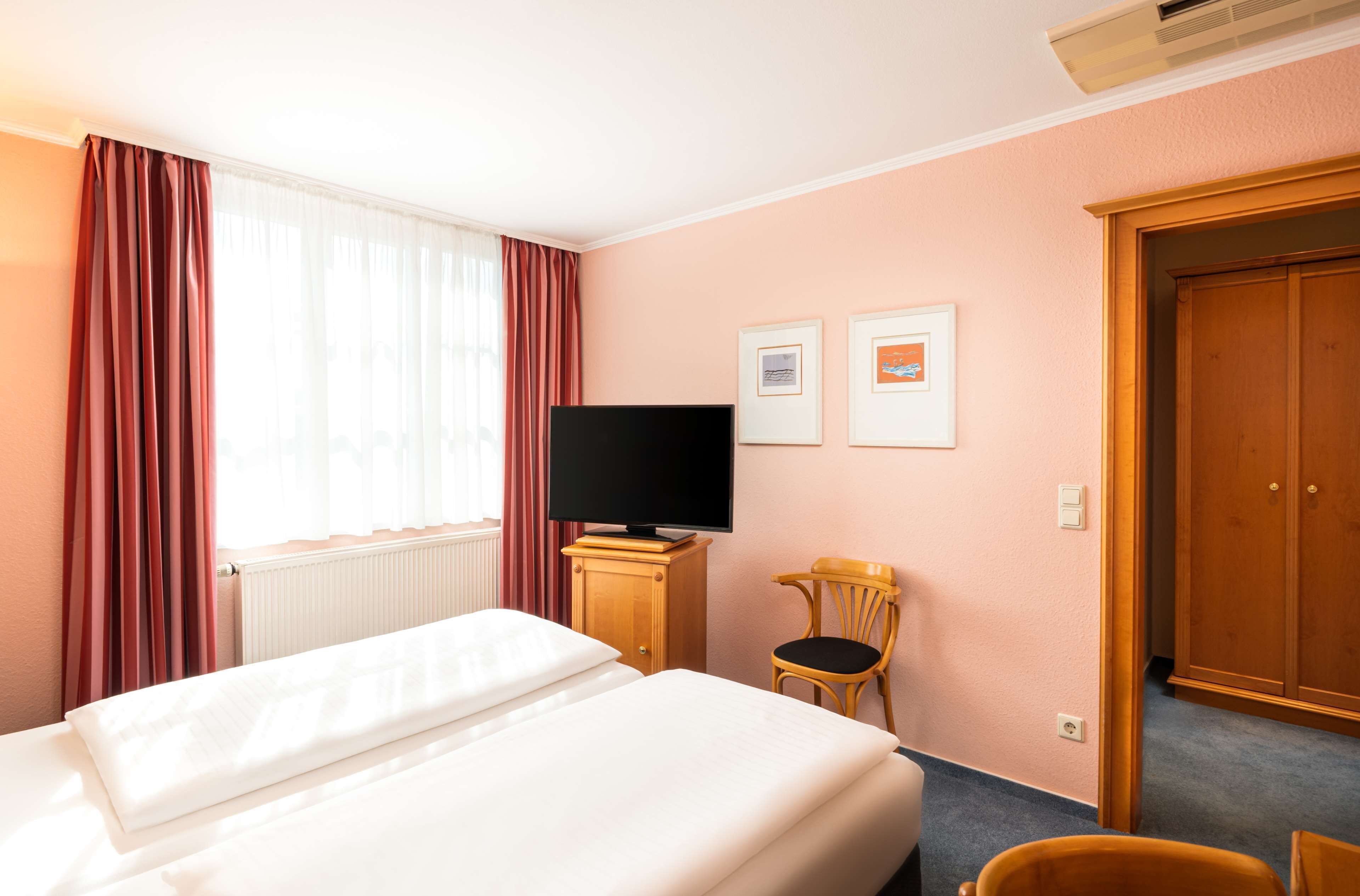 Una habitación de hotel con una cama, un televisor sobre un soporte de madera, una silla y una puerta.