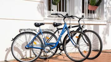Two bicycles parked against a white building with a window and potted plants.