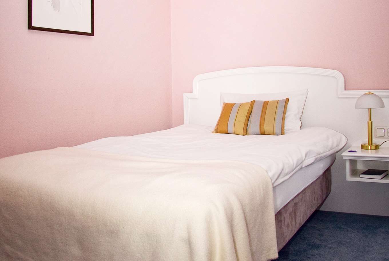 A neatly made bed with white bedding and two striped pillows, a bedside table with a lamp, and a framed picture on the wall.