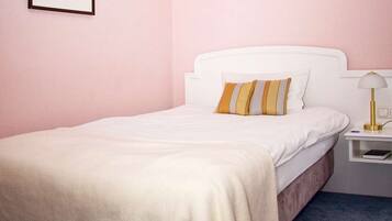 A neatly made bed with white bedding and two striped pillows, a bedside table with a lamp, and a framed picture on the wall.