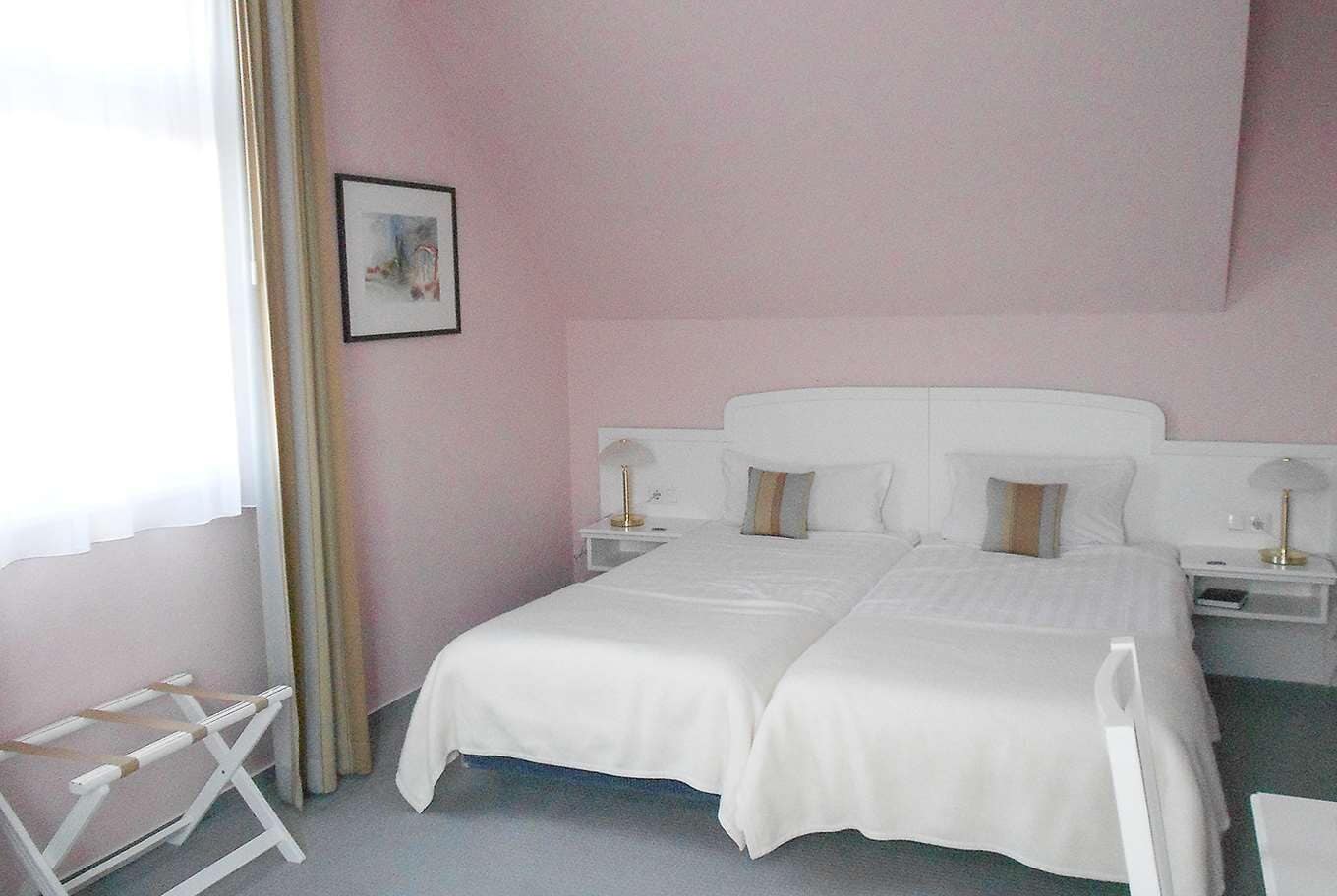 A hotel room with a large bed, two bedside tables, a chair, and a window with sheer curtains.