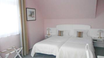 A hotel room with a large bed, two bedside tables, a chair, and a window with sheer curtains.