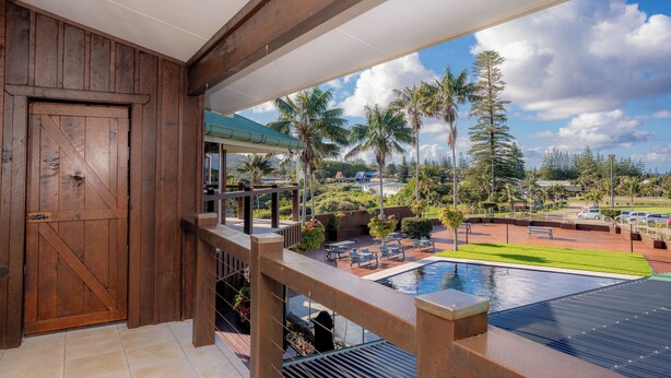 Ein Holzbalkon mit Blick auf ein Schwimmbecken, Palmen und eine ferne Landschaft.