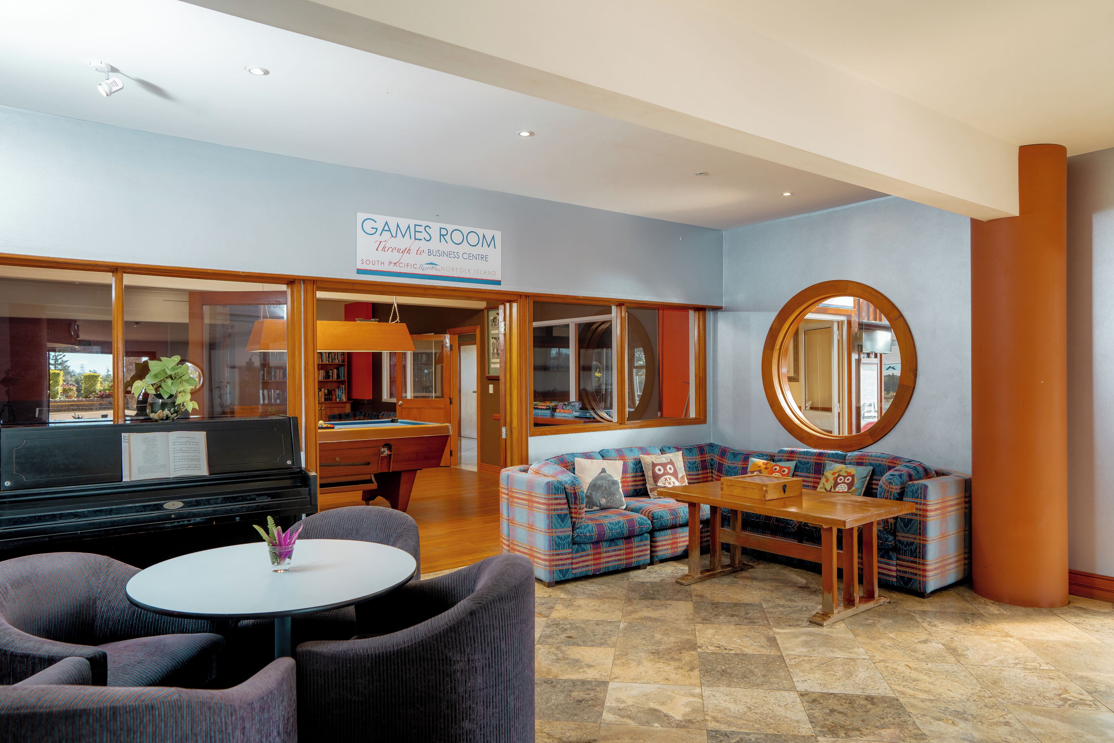 A spacious room with a piano, a sofa set, a round mirror, and a sign reading "GAMES ROOM".