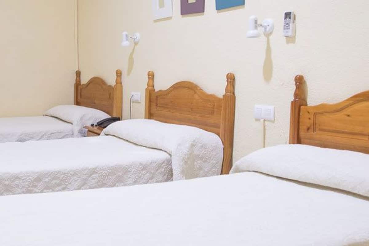 A hotel room with three single beds, wooden headboards, and a small bedside table.