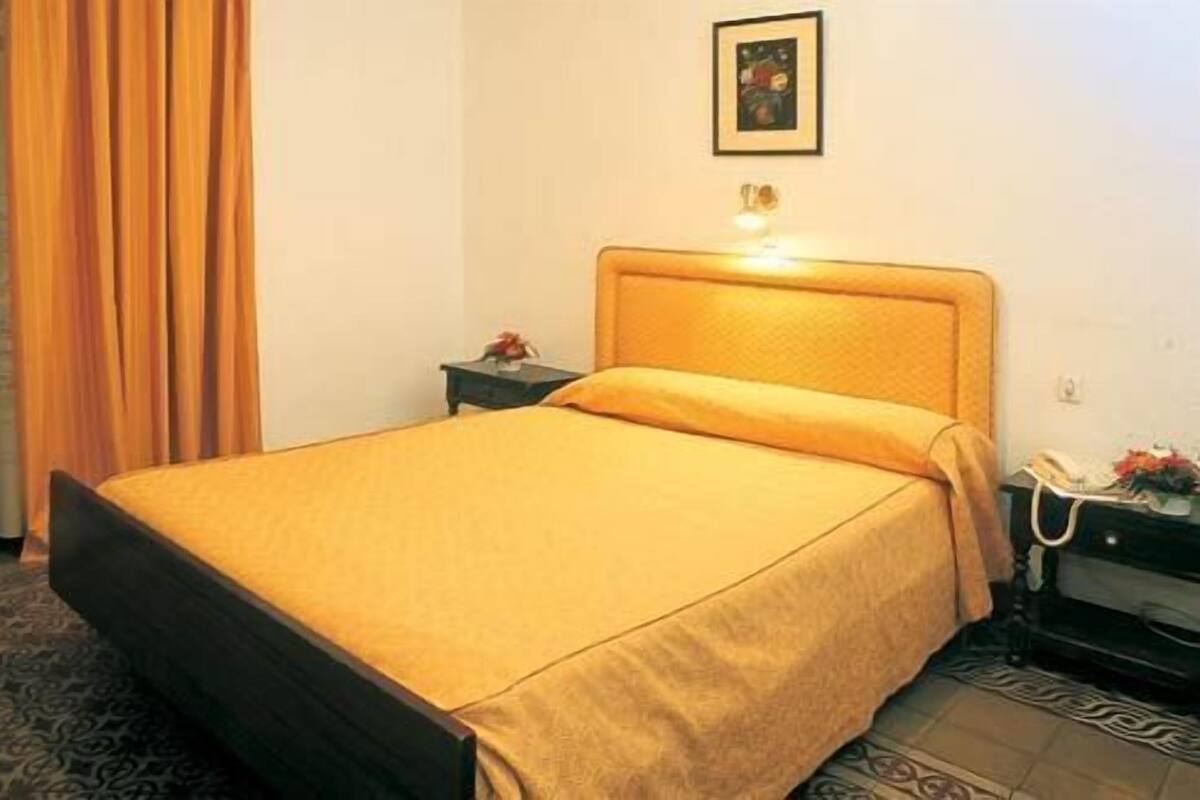 A bed with a headboard, a nightstand with a lamp, and a framed picture on the wall.