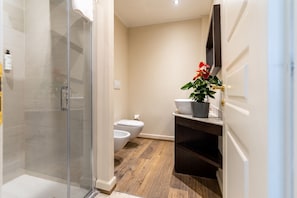 Une salle de bain avec une douche à parois de verre, des toilettes, un lavabo agrémenté d’une plante en pot et un meuble en bois foncé.