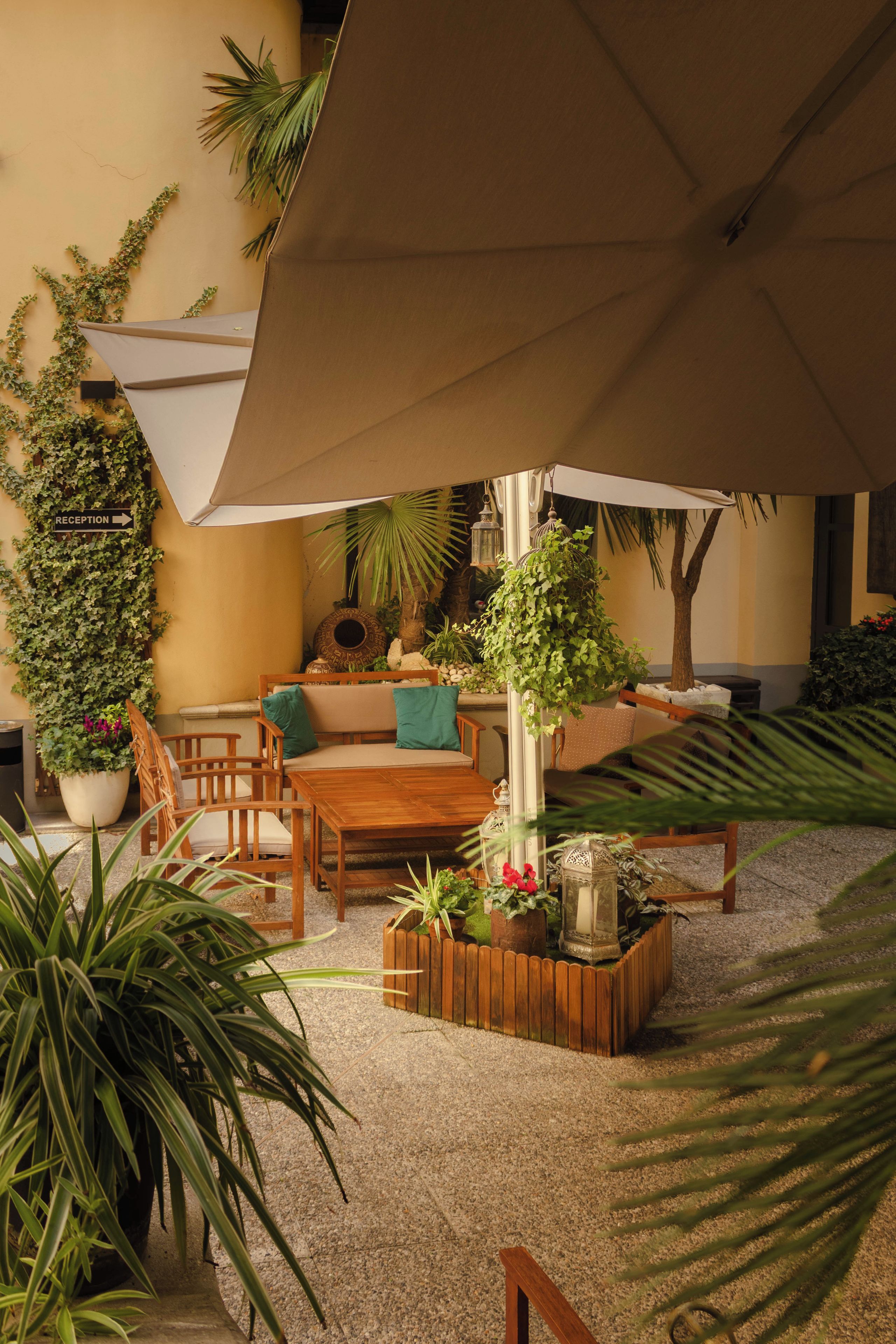 A patio area with a wooden table, chairs, a reception sign, and various potted plants.