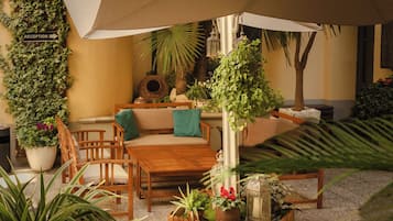 A patio area with a wooden table, chairs, a reception sign, and various potted plants.