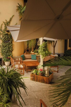 Un espace patio aménagé avec une table en bois, des chaises, un panneau d’accueil et diverses plantes en pot.