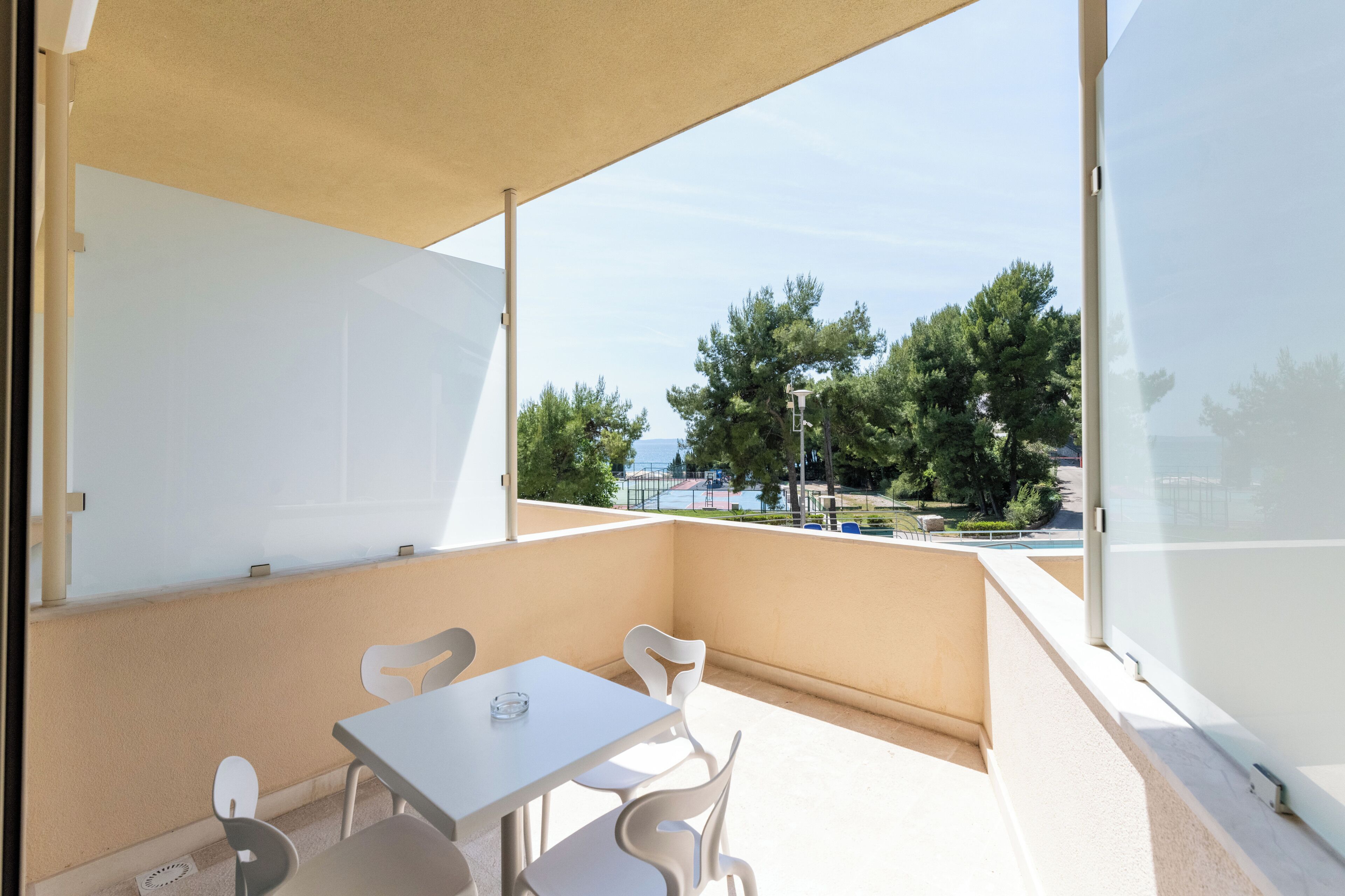 En balkon med et bord og stole, udsigt til træer og et vandområde.