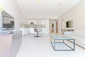 A modern kitchen with white cabinets, a dining area with a glass table, and a living room with a white sofa and a glass coffee table. - The Residence (Podstrana)