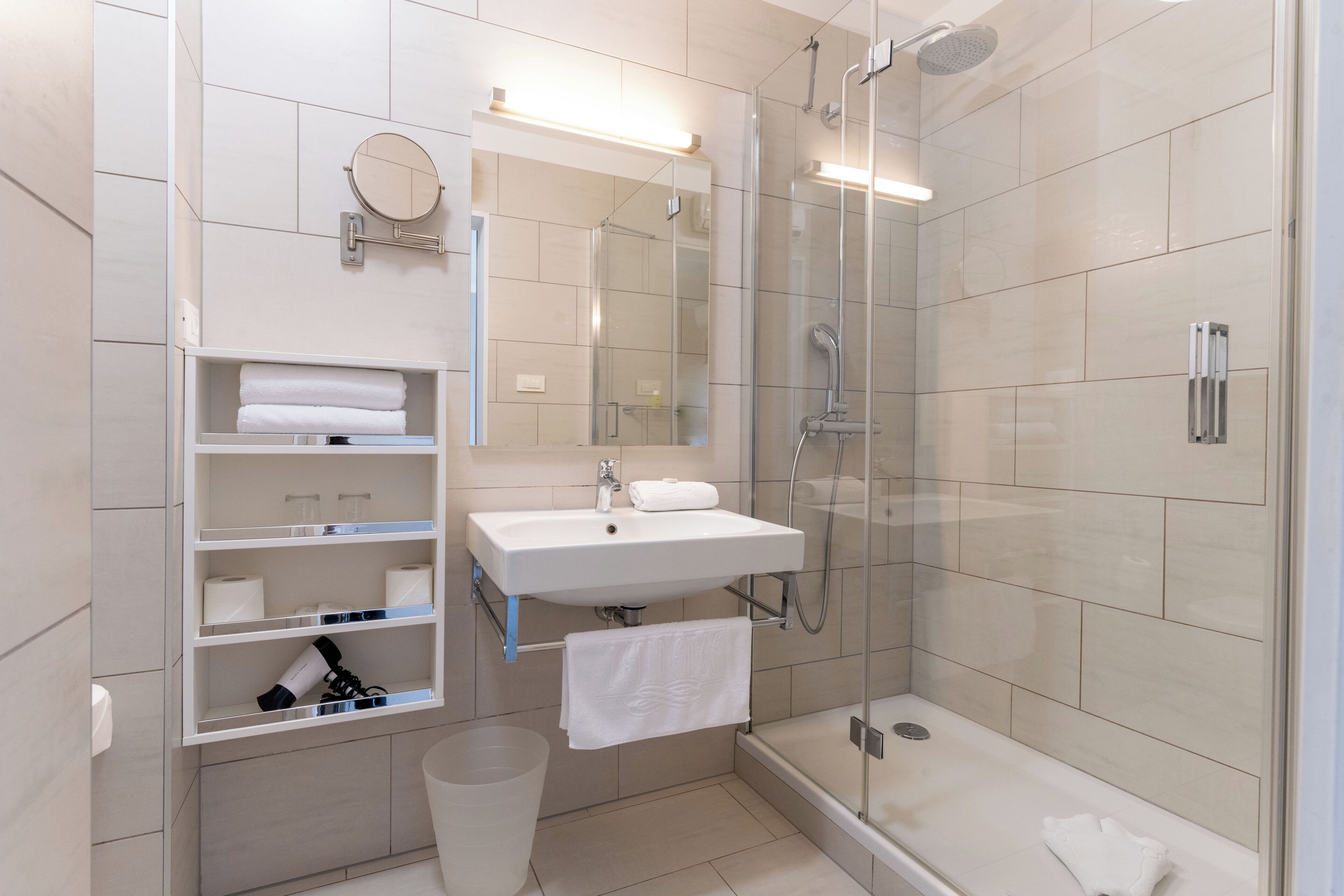 Ein modernes Badezimmer mit einer Duschkabine aus Glas, einem weißen Waschbecken und einer integrierten Ablage mit Handtüchern.