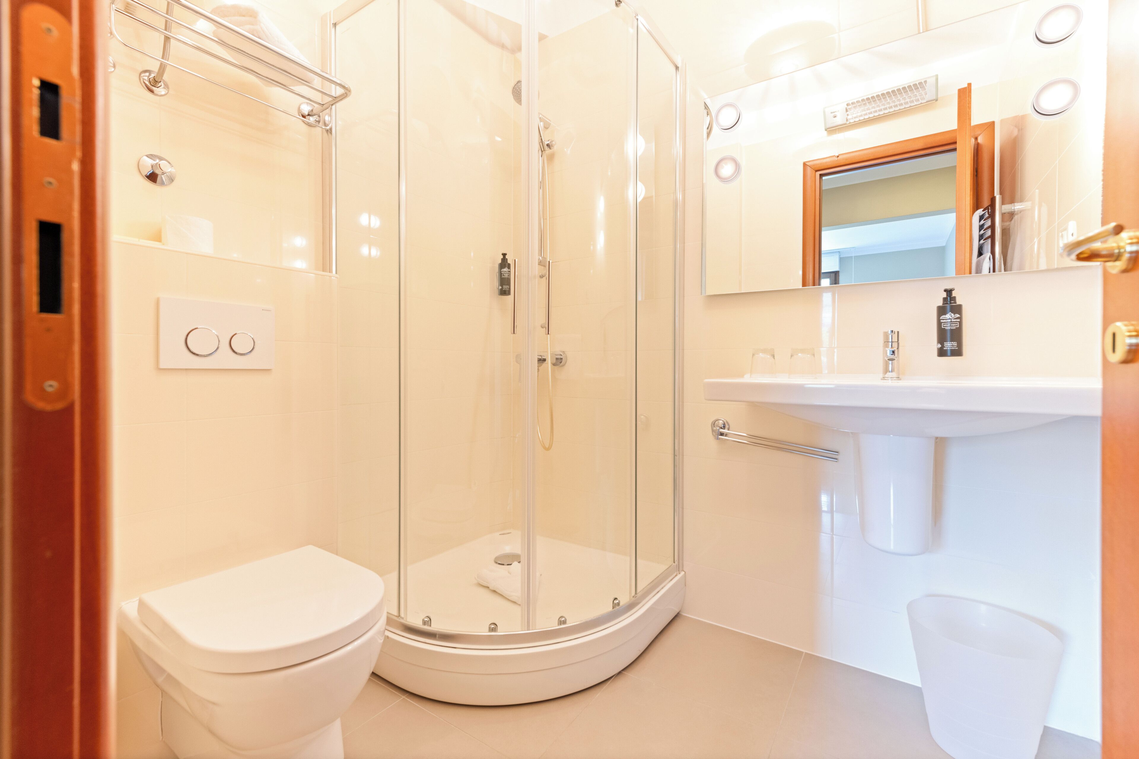 Une salle de bain moderne avec une douche à parois de verre, des toilettes blanches et un lavabo surmonté d’un miroir.