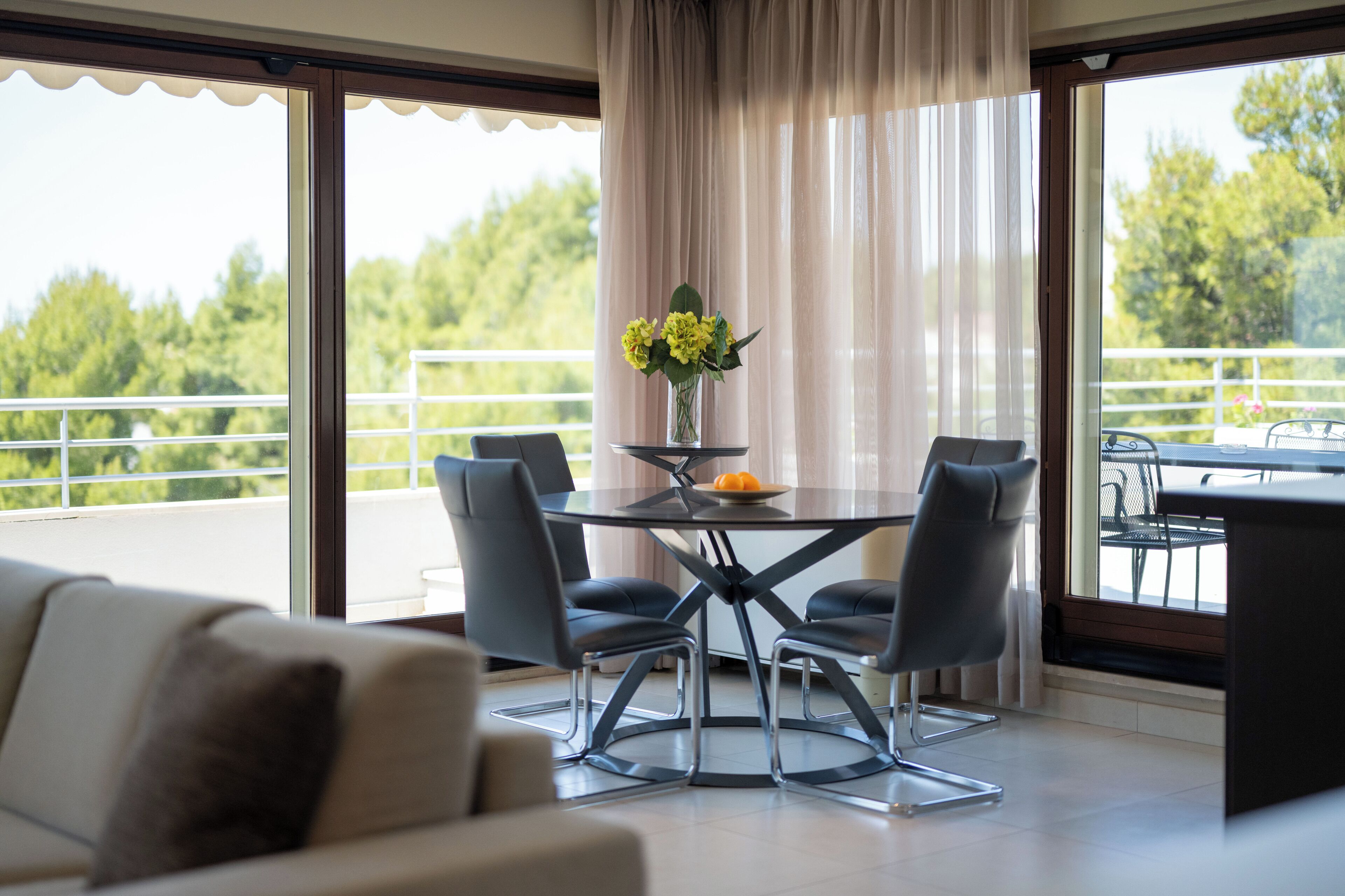 A modern dining area with a glass table, four chairs, and a vase with flowers.