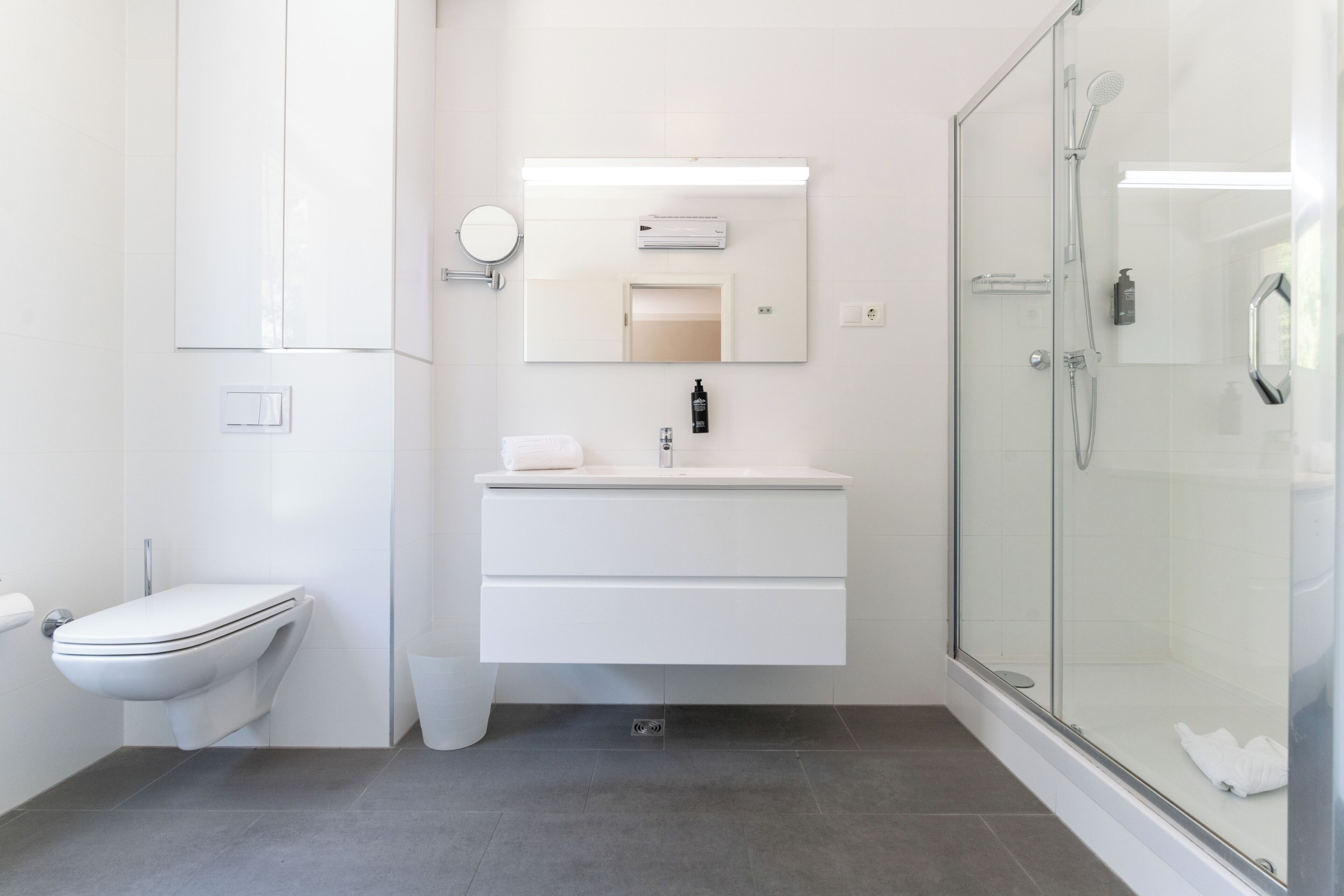 Een moderne badkamer met toilet, een wastafel met spiegel en een douche met glazen wanden.