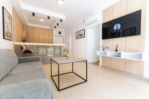A modern reception area with a grey sofa, a glass-top table, wooden cabinets, and a mounted TV displaying the 'AURIANE' logo. - The Residence (Podstrana)