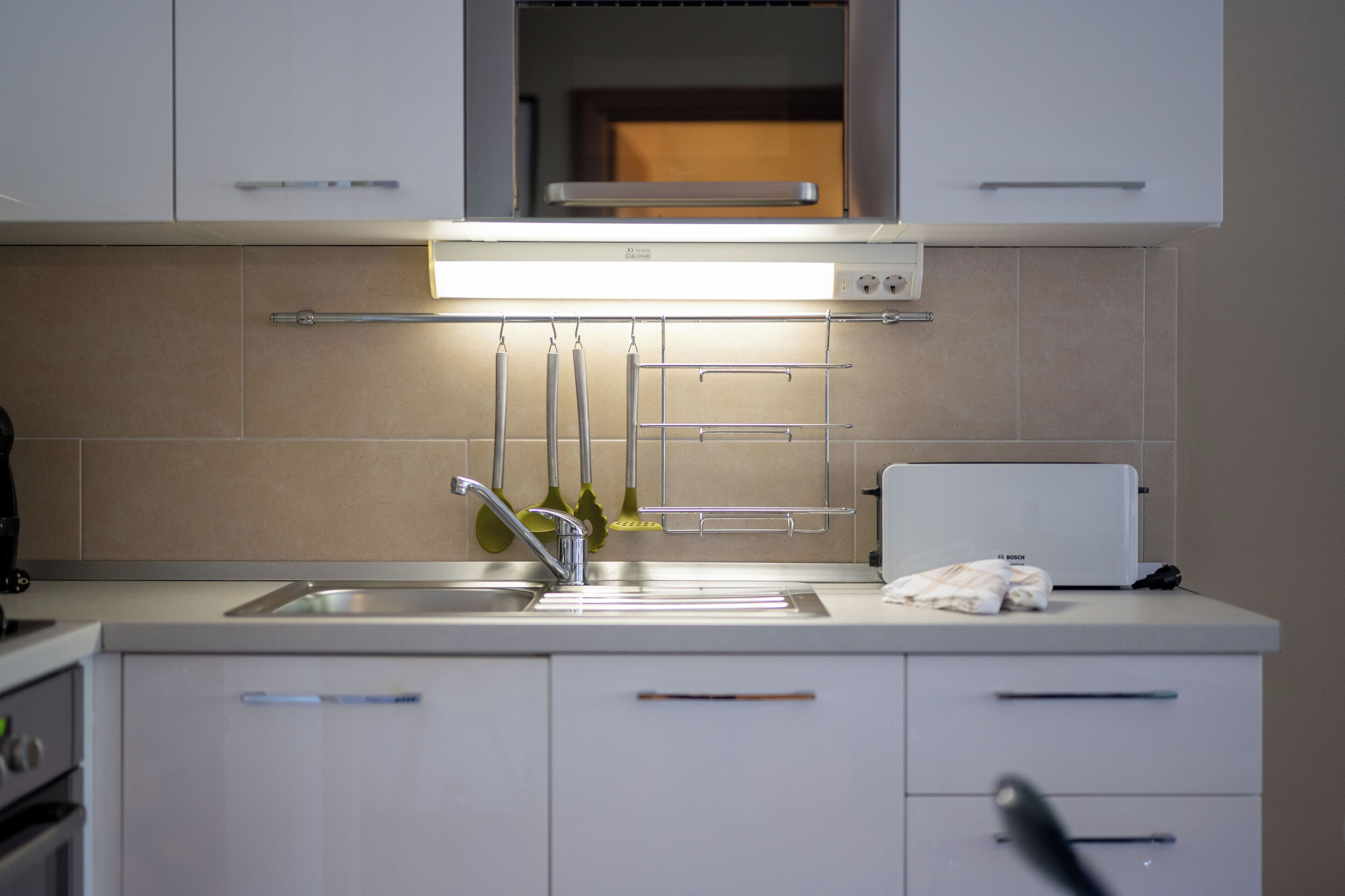 A modern kitchen with a stainless steel sink, a built-in oven, and a white countertop.
