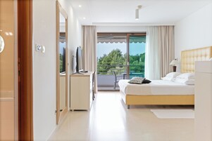 Una habitación de hotel moderna con cama, escritorio, televisión y balcón con vistas a árboles.