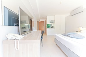A modern hotel room with a large mirror, a desk with a telephone, a bed with pillows, a kitchenette, and a bathroom. - The Residence (Podstrana)