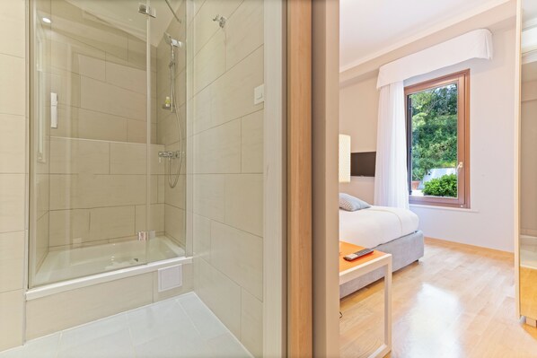 A modern bathroom with a glass-enclosed shower, a bathtub, and a wooden floor.