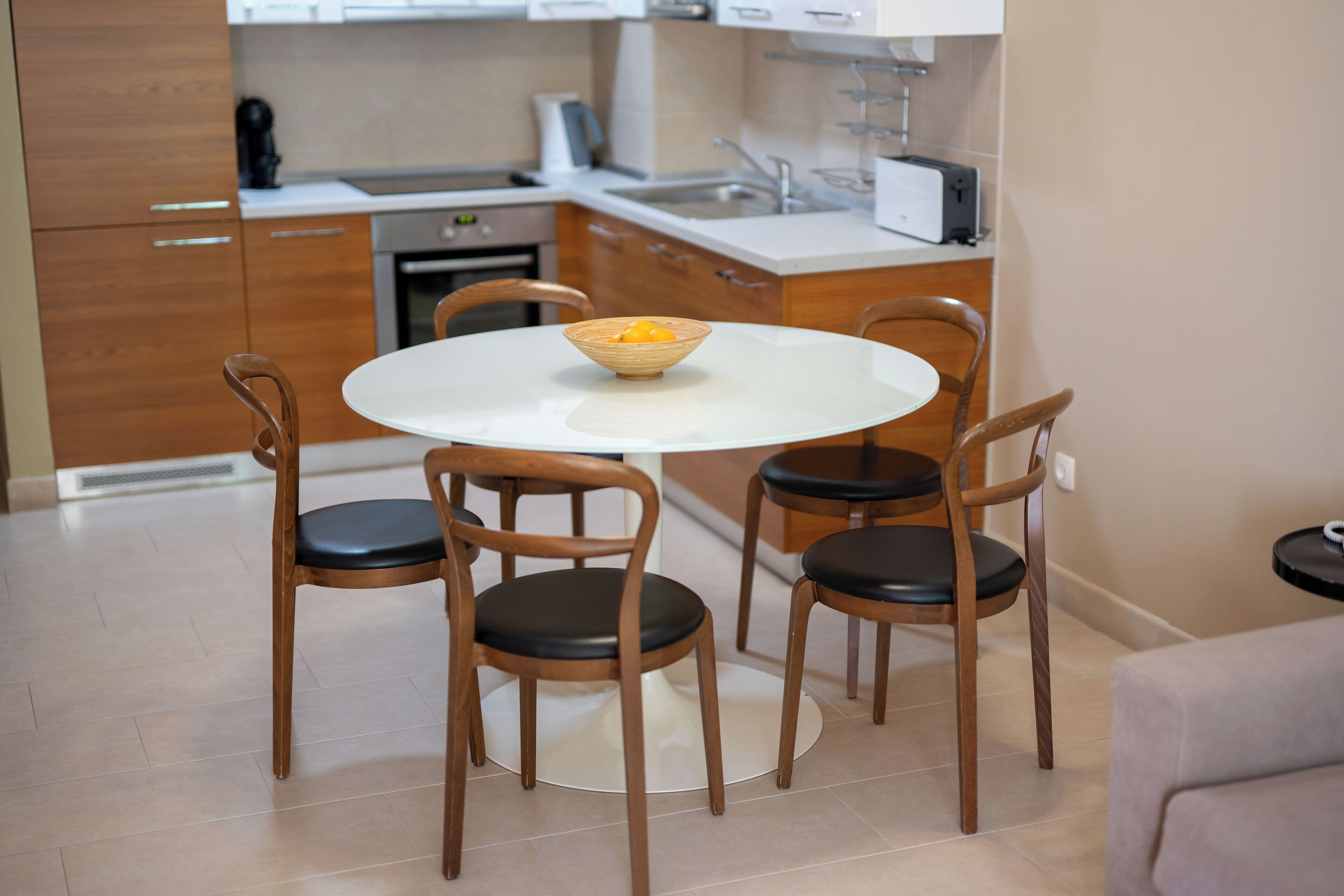 Une cuisine moderne avec des meubles en bois, un plan de travail blanc et une table de salle à manger ronde, accompagnée de quatre chaises.