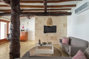 Una sala de estar con pared de piedra, televisor montado, una mesa de centro de madera, sofá gris y lámpara colgante.