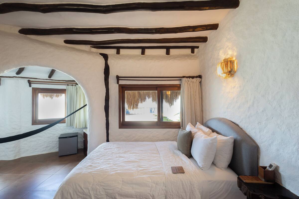 A bedroom with a bed, a nightstand, a lamp, a window with curtains, and a view of the outside.