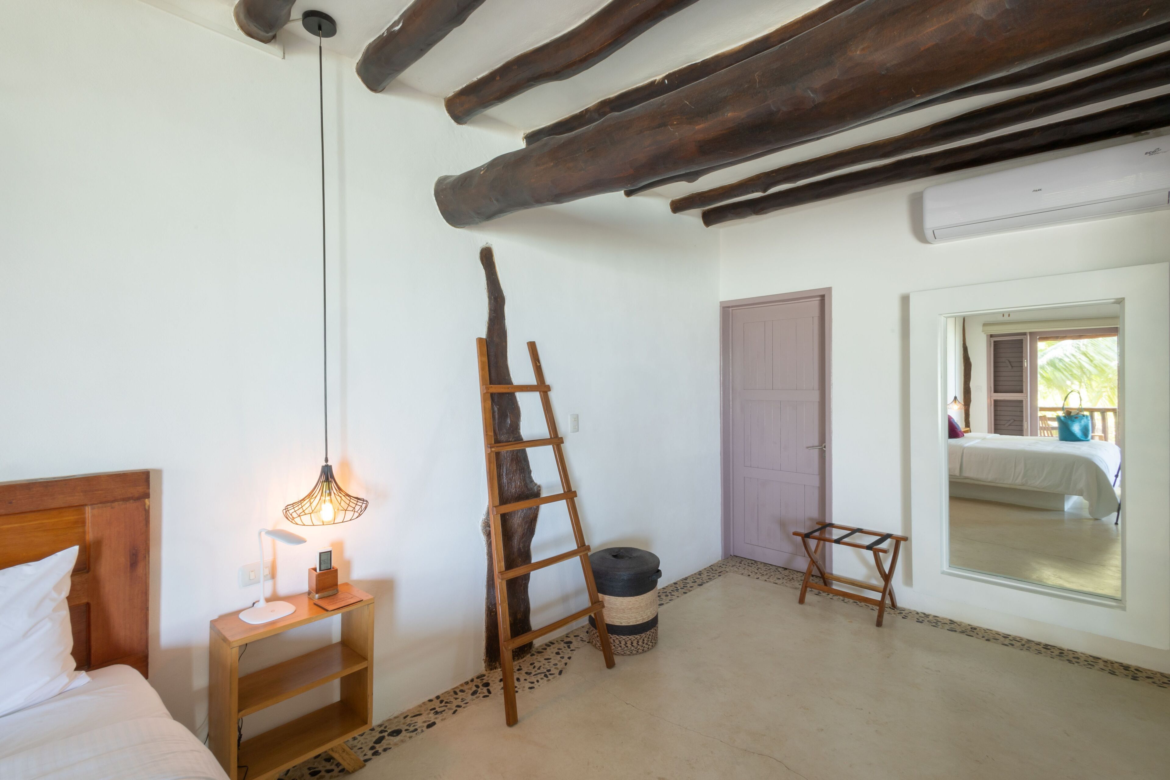 A bedroom with a wooden ladder, a bedside table with a lamp, a window with a view, and a door.