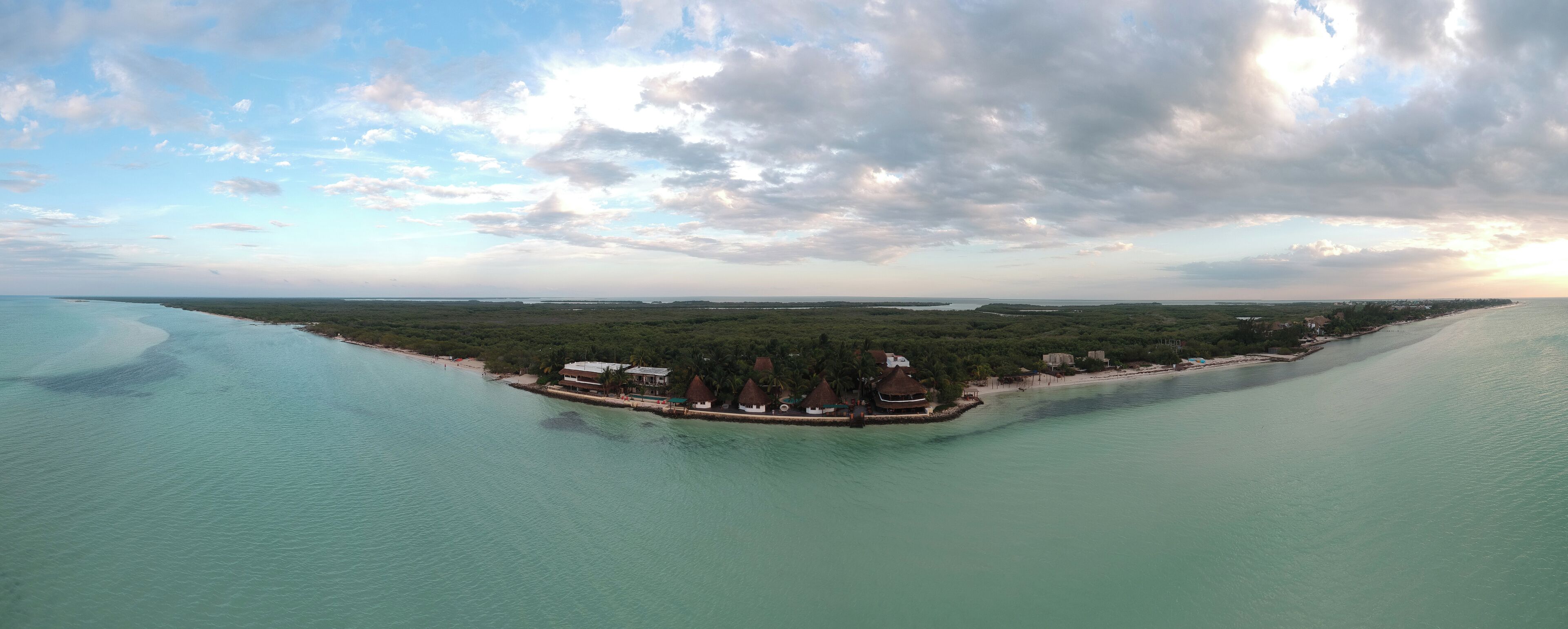 An aerial view of a coastal resort with overwater bungalows, clear turquoise waters, and a distant shoreline.