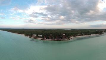 An aerial view of a coastal resort with overwater bungalows, clear turquoise waters, and a distant shoreline.