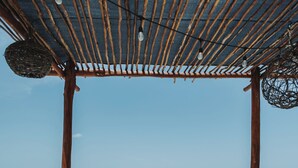 A beach view with wooden lounge chairs and a covered area with hanging lights. - Las Nubes de Holbox (Isla Holbox)