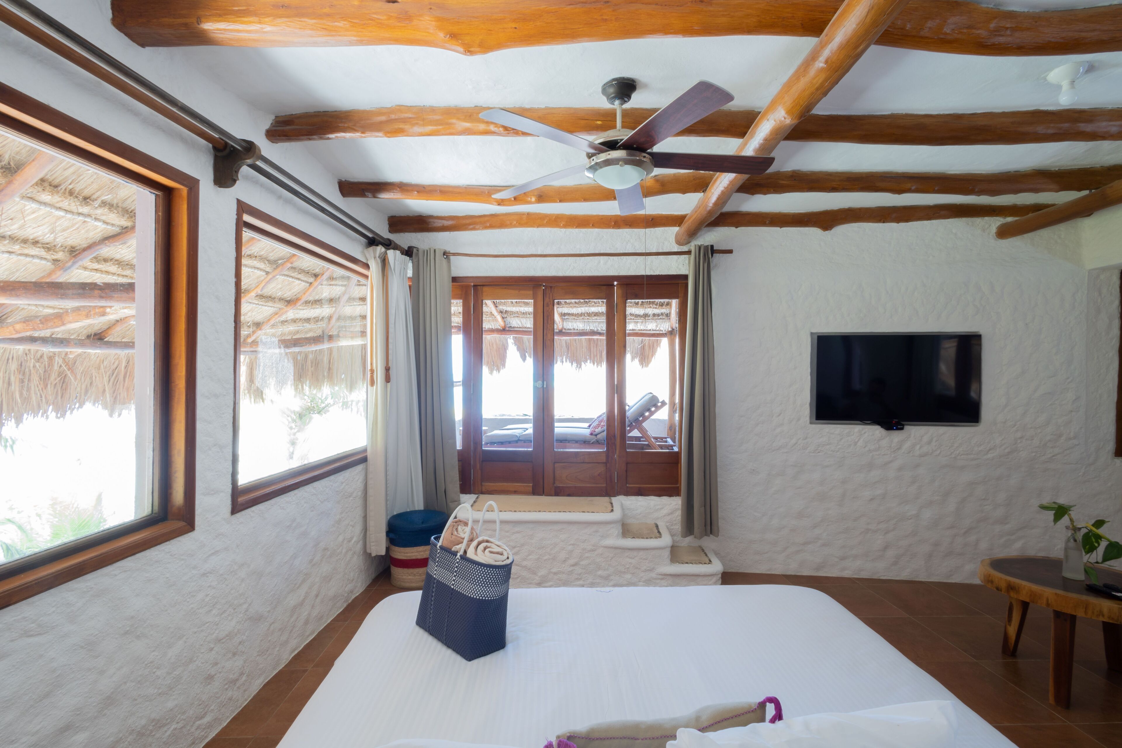 A bedroom with a large bed, a ceiling fan, a TV, and a view of the outside.