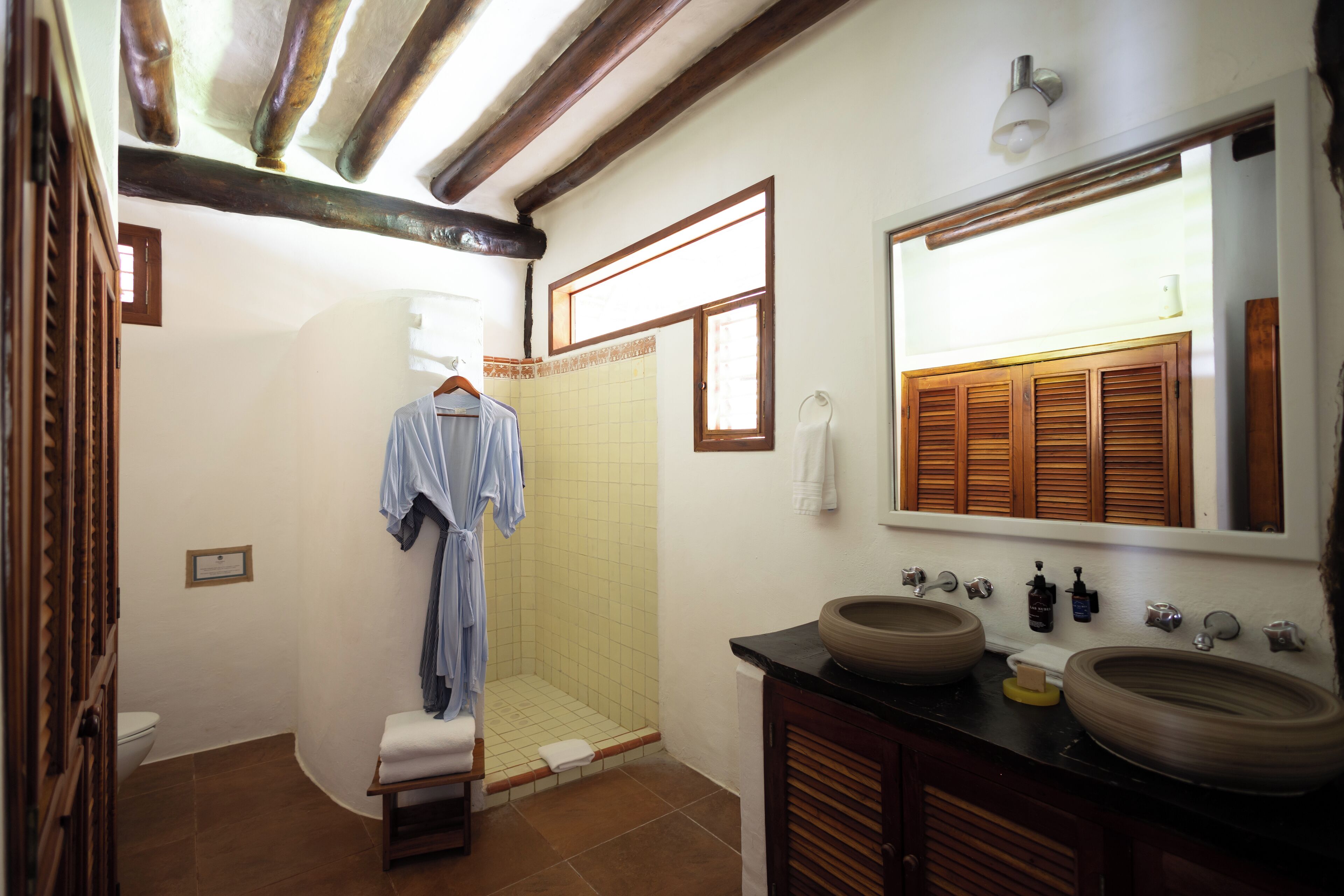 A bathroom with a shower, two sinks, wooden cabinets, and a large mirror.