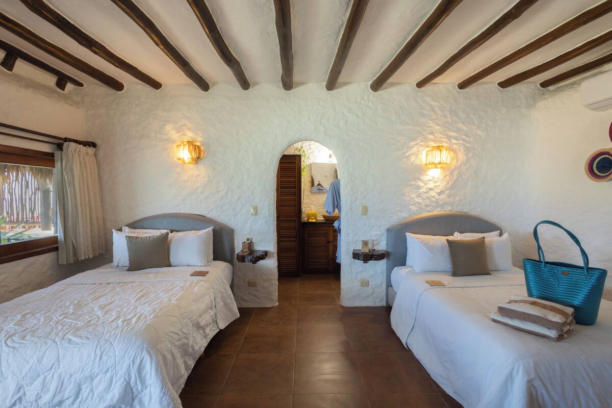 A bedroom with two beds, a wooden ceiling, and a view through an archway.