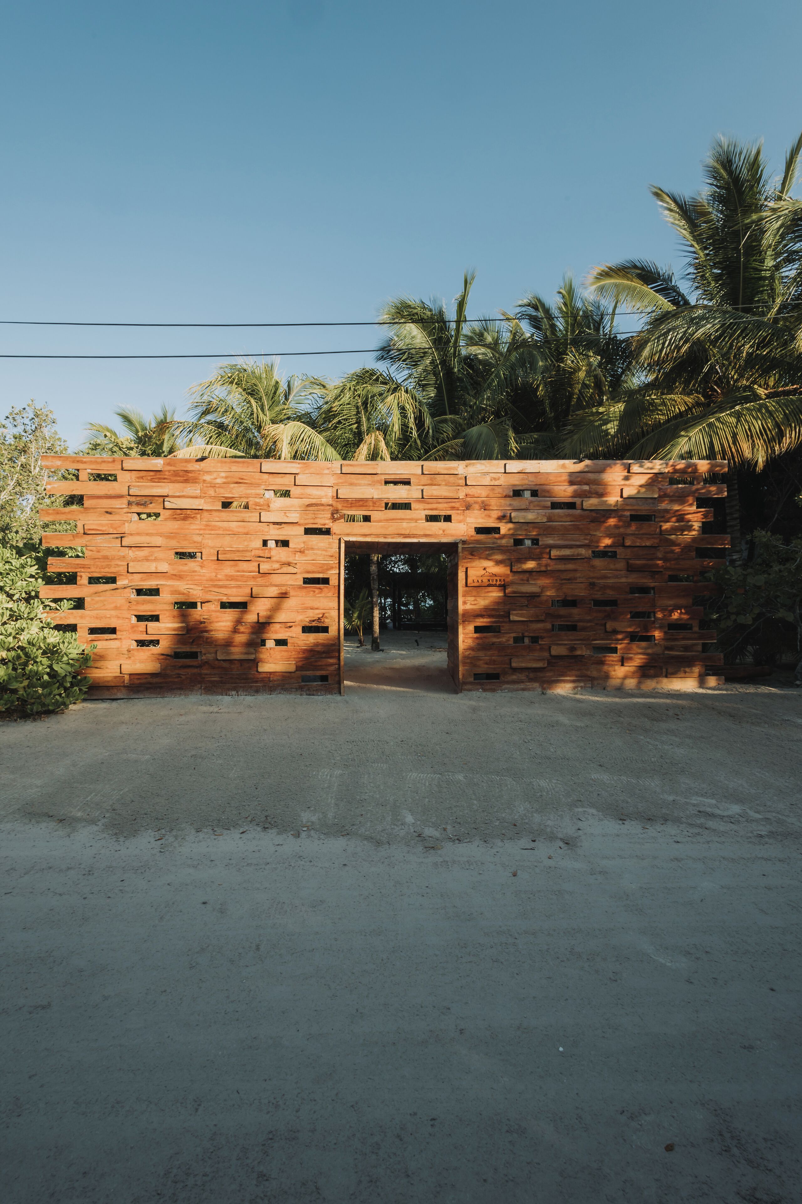 A wooden structure with a door, surrounded by palm trees and a clear sky.