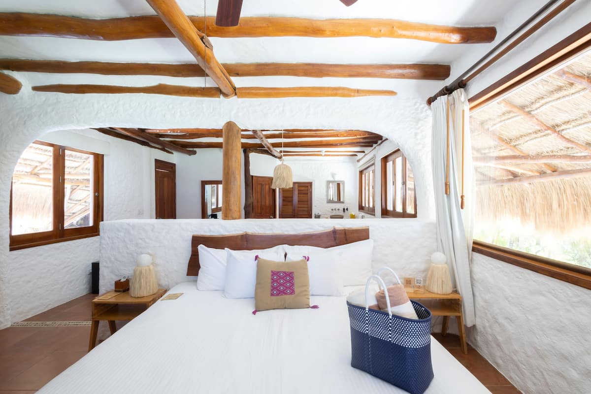 A bedroom with a large bed, wooden beams, white walls, and a window with a view.
